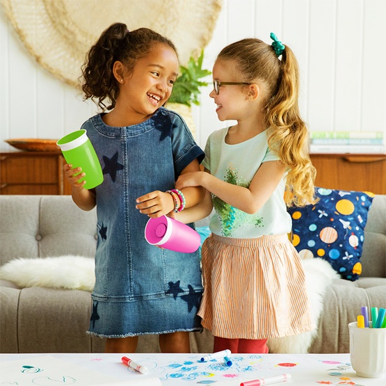 Two little girls, each holding a Munchkin Miracle® 360° Cup